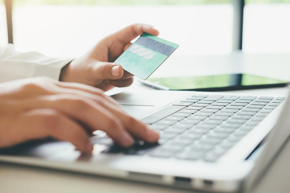 Femme tenant une carte de crédit tout en utilisant un ordinateur portable