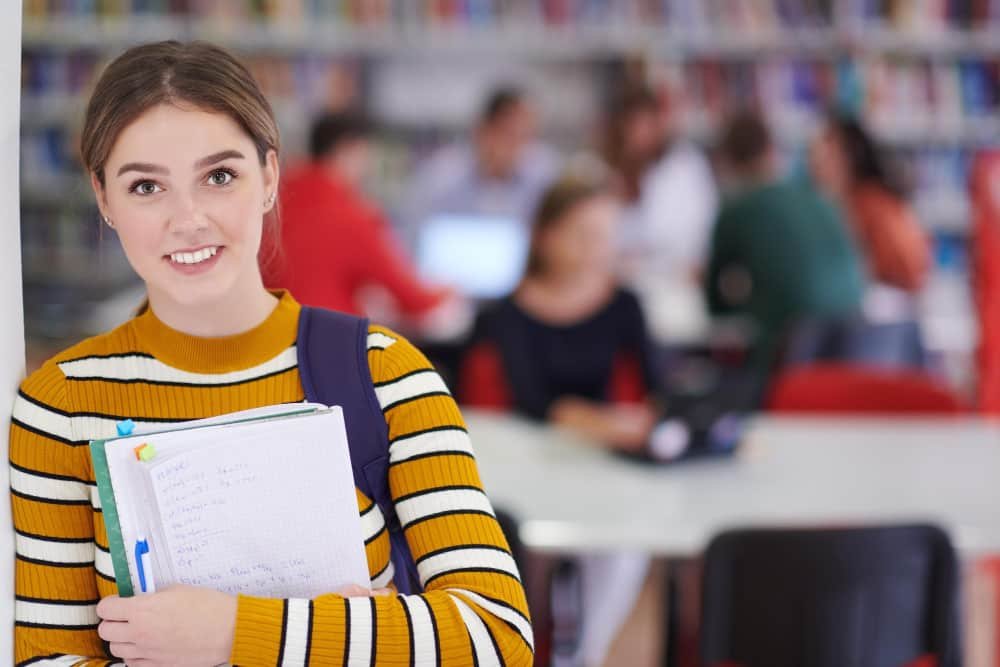 Eleve utilise un cahier et une bibliothèque scolaire