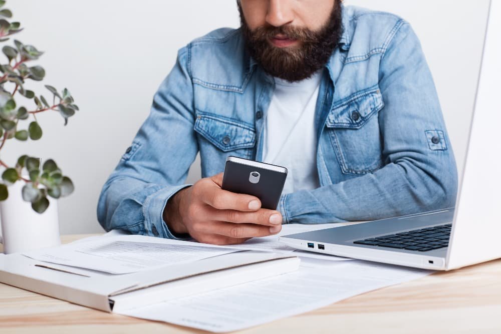 Homme barbu en chemise en jean devant son pc portable